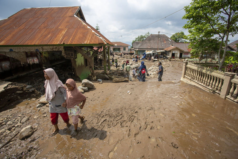 5月12日，在印度尼西亚西苏门答腊省，人们经过被洪水损毁的房屋。新华社发（安德里·马迪安赛亚摄）.jpeg